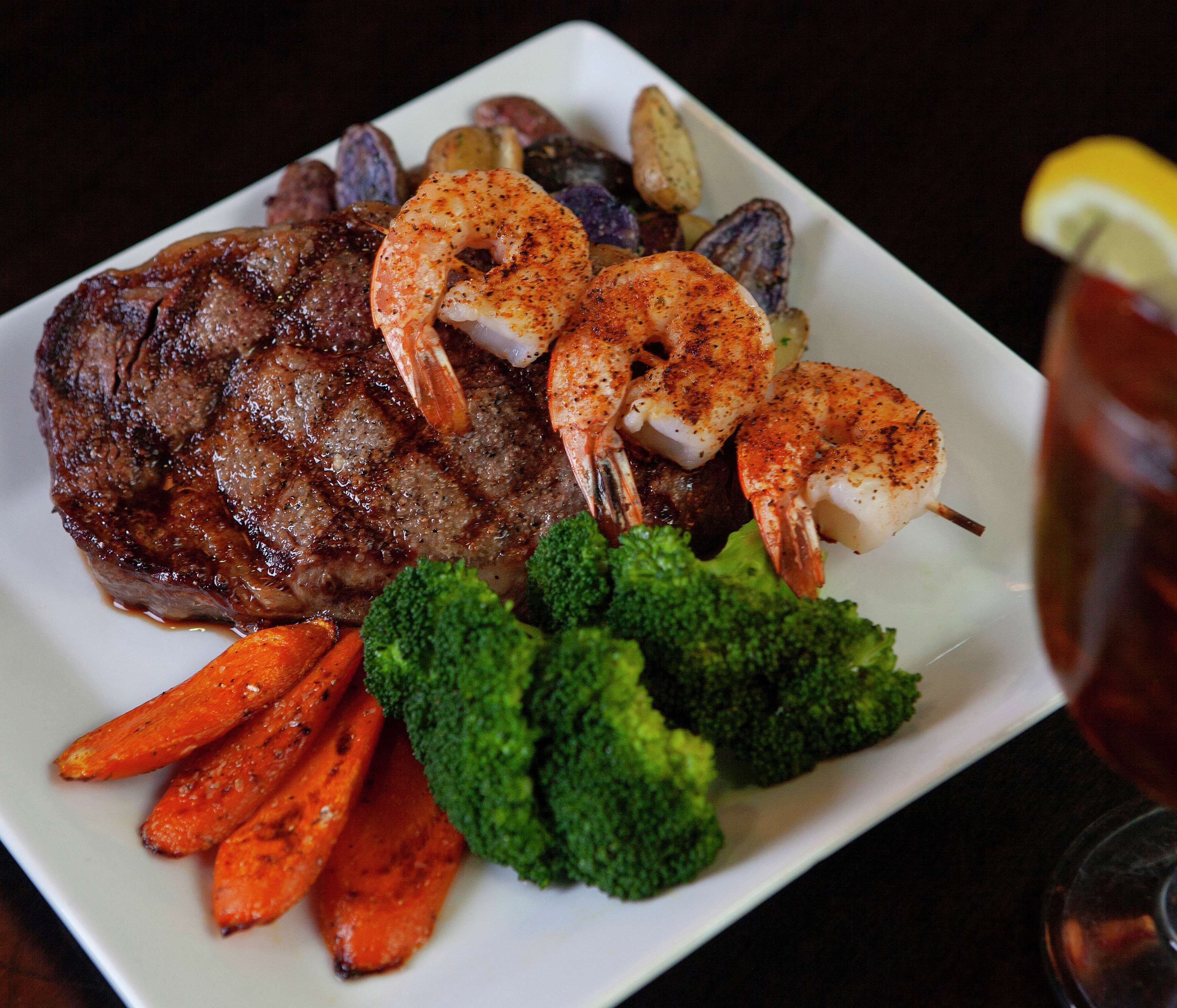 Un plato con bistec, camarones, zanahorias y brócoli.