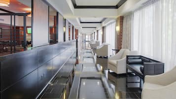 Un hall de hotel con un mostrador de recepción alargado, zona de estar con sofás y suelo de baldosas.