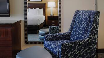 A hotel room with a bed, a chair, a desk, and a mirror.