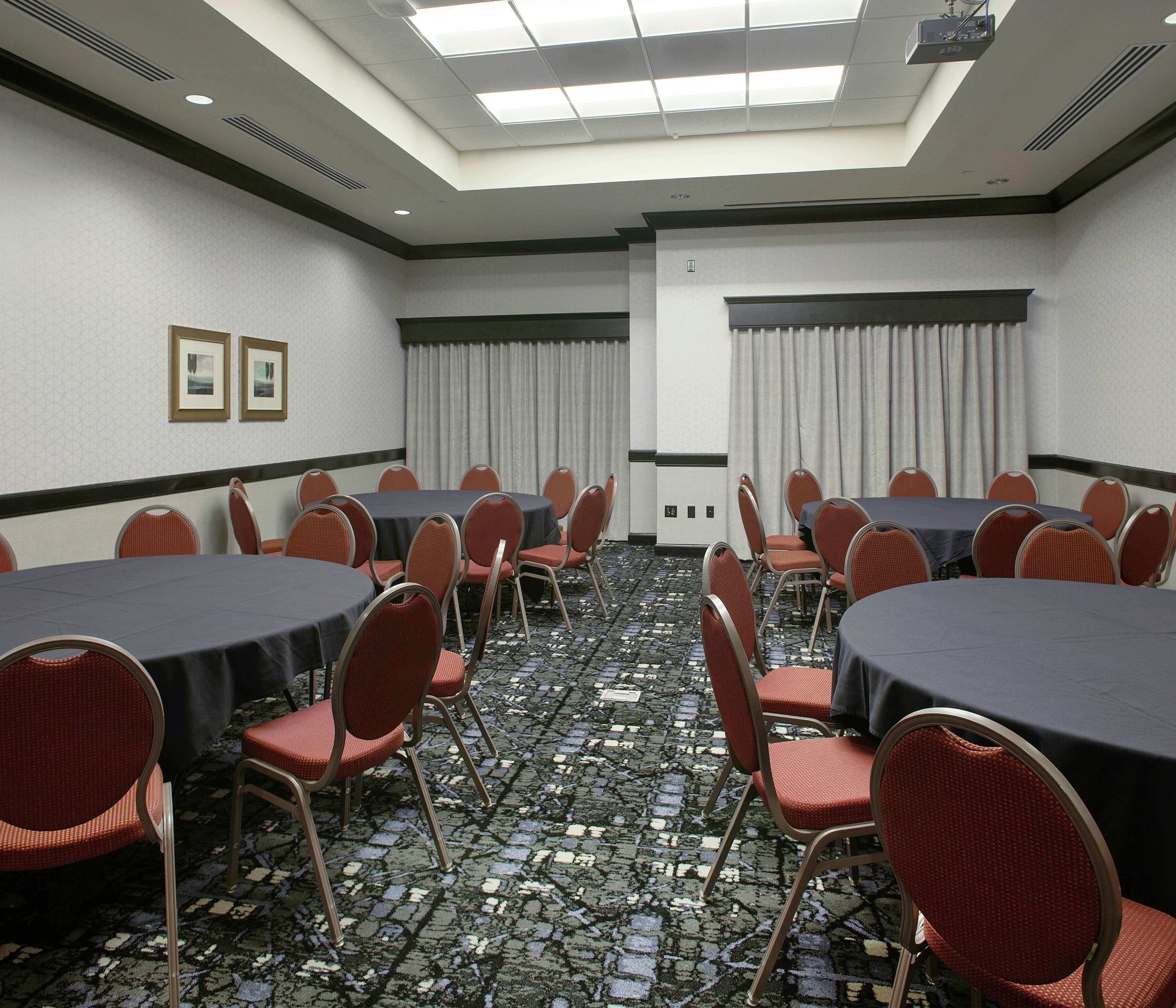 Un salón de conferencias con varias mesas y sillas, una alfombra estampada y un techo con tragaluces.