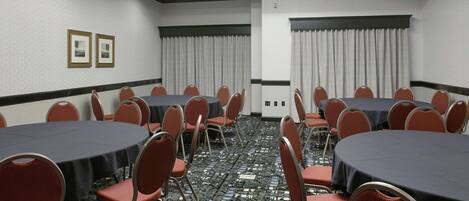 Un salón de conferencias con varias mesas y sillas, una alfombra estampada y un techo con tragaluces.