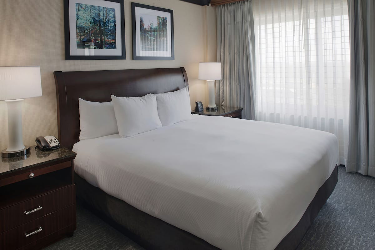A large bed with white linens, two bedside tables with lamps, a telephone, and framed pictures on the wall.