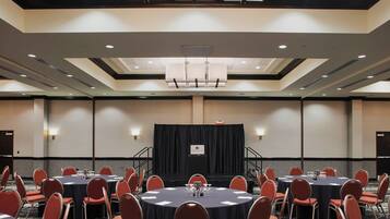 A conference room with multiple round tables and chairs, a stage with a backdrop, and a modern ceiling design.