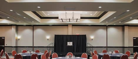 Une salle de conférence dotée de plusieurs tables rondes et de chaises, d’une scène avec un décor en fond et d’un plafond au design moderne.
