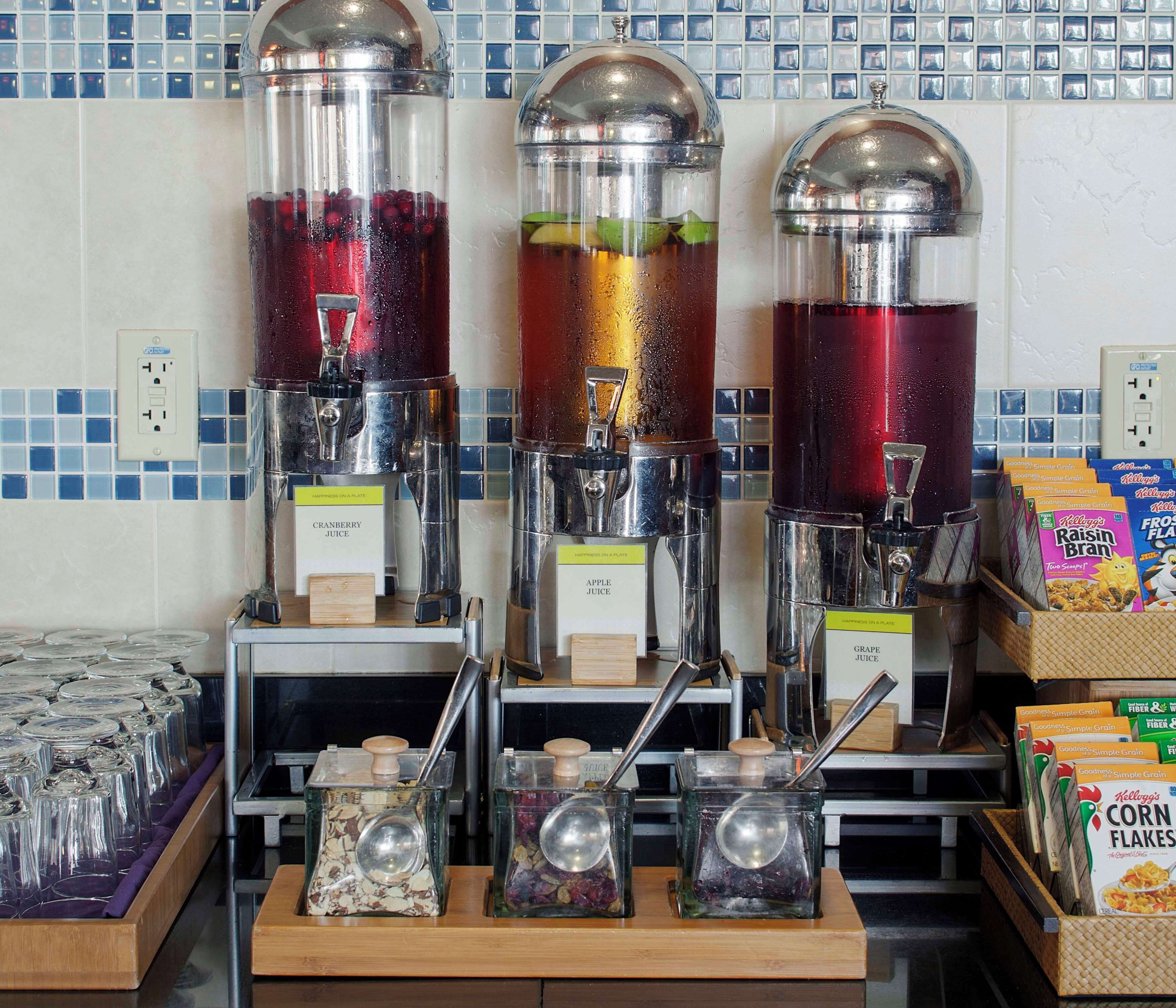 Tres dispensadores de bebidas con etiquetas para jugo de arándano, manzana y uva.