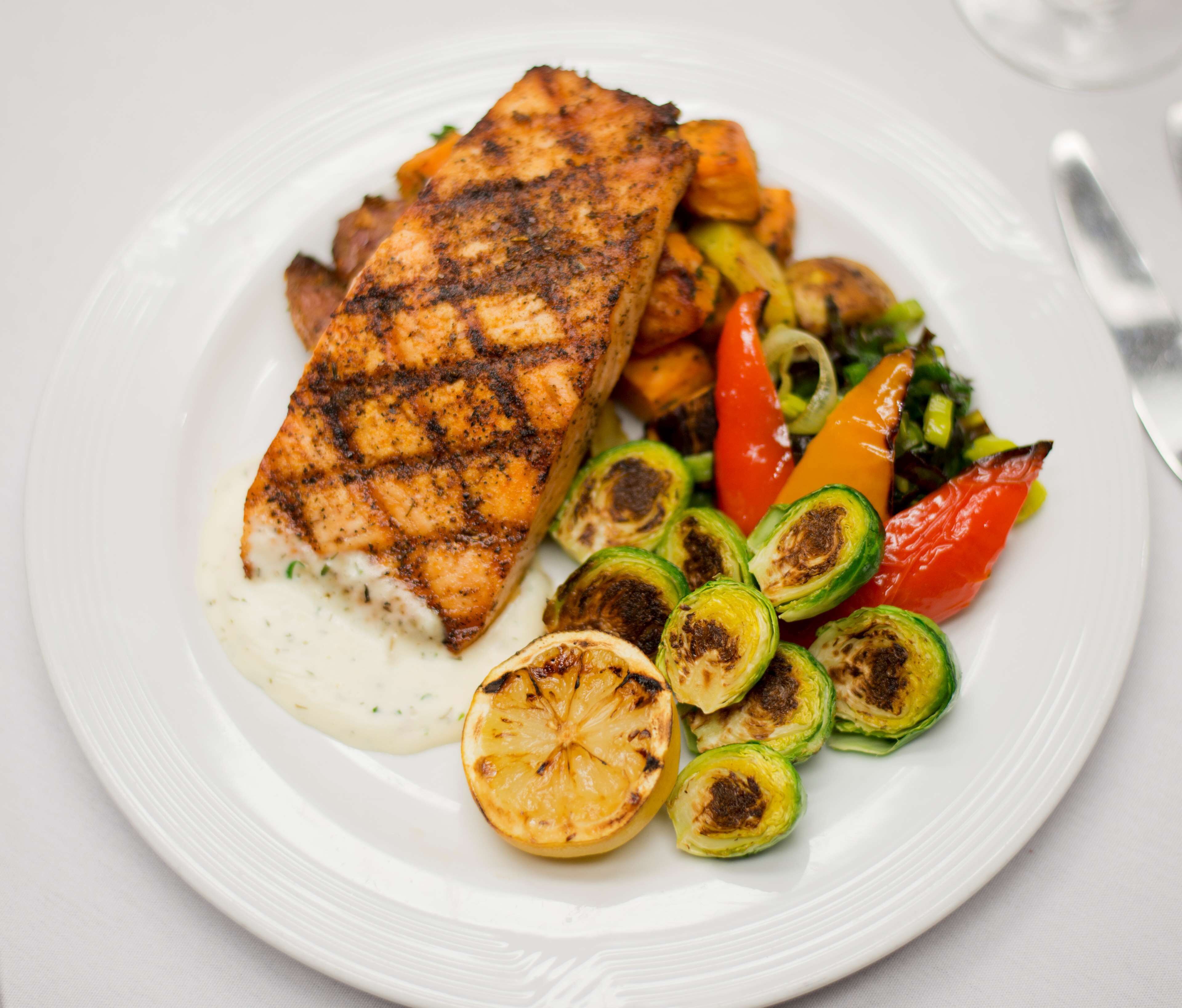 A plate with grilled fish, roasted vegetables, and a slice of lemon.