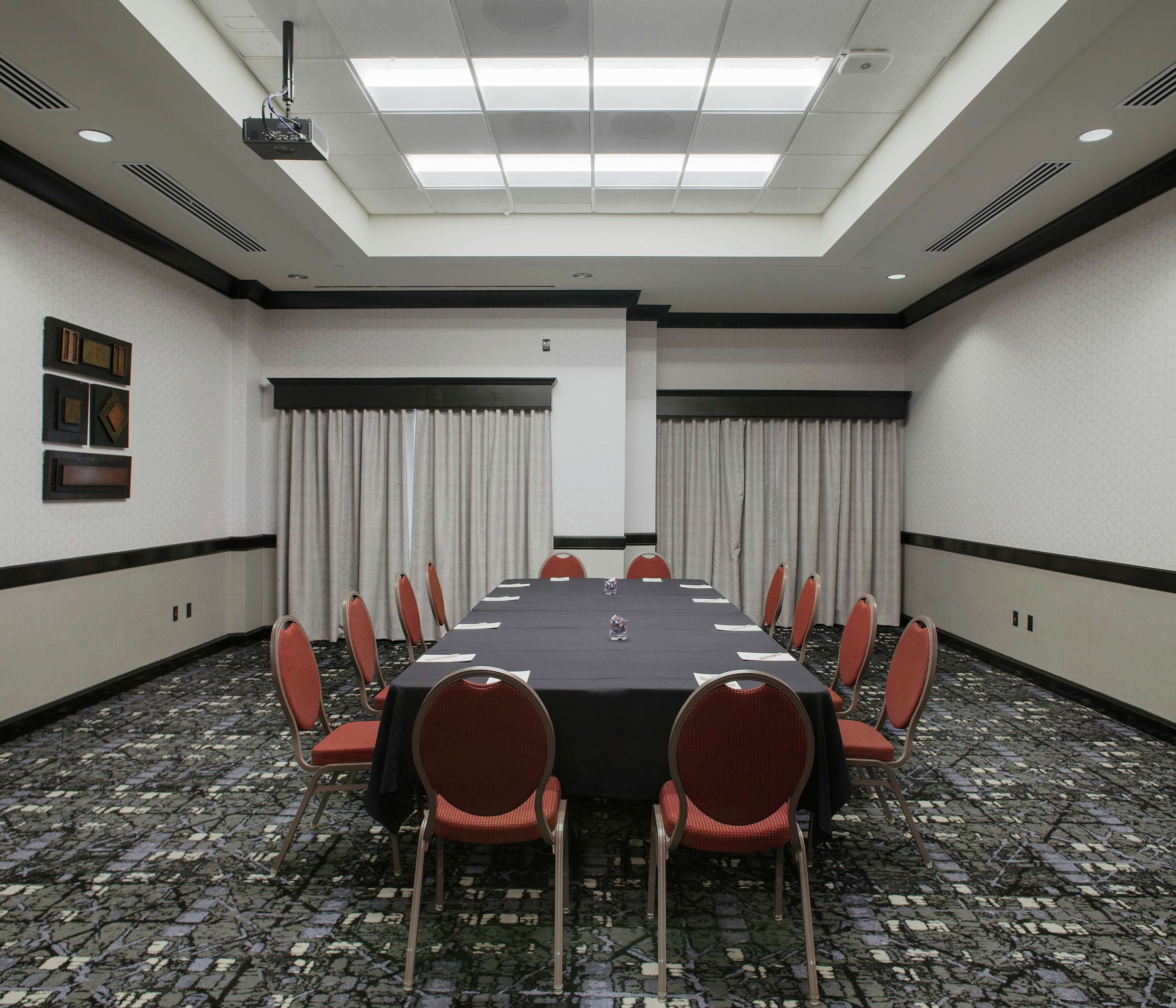 A conference room with a long table, red chairs, a projector, and a carpeted floor.