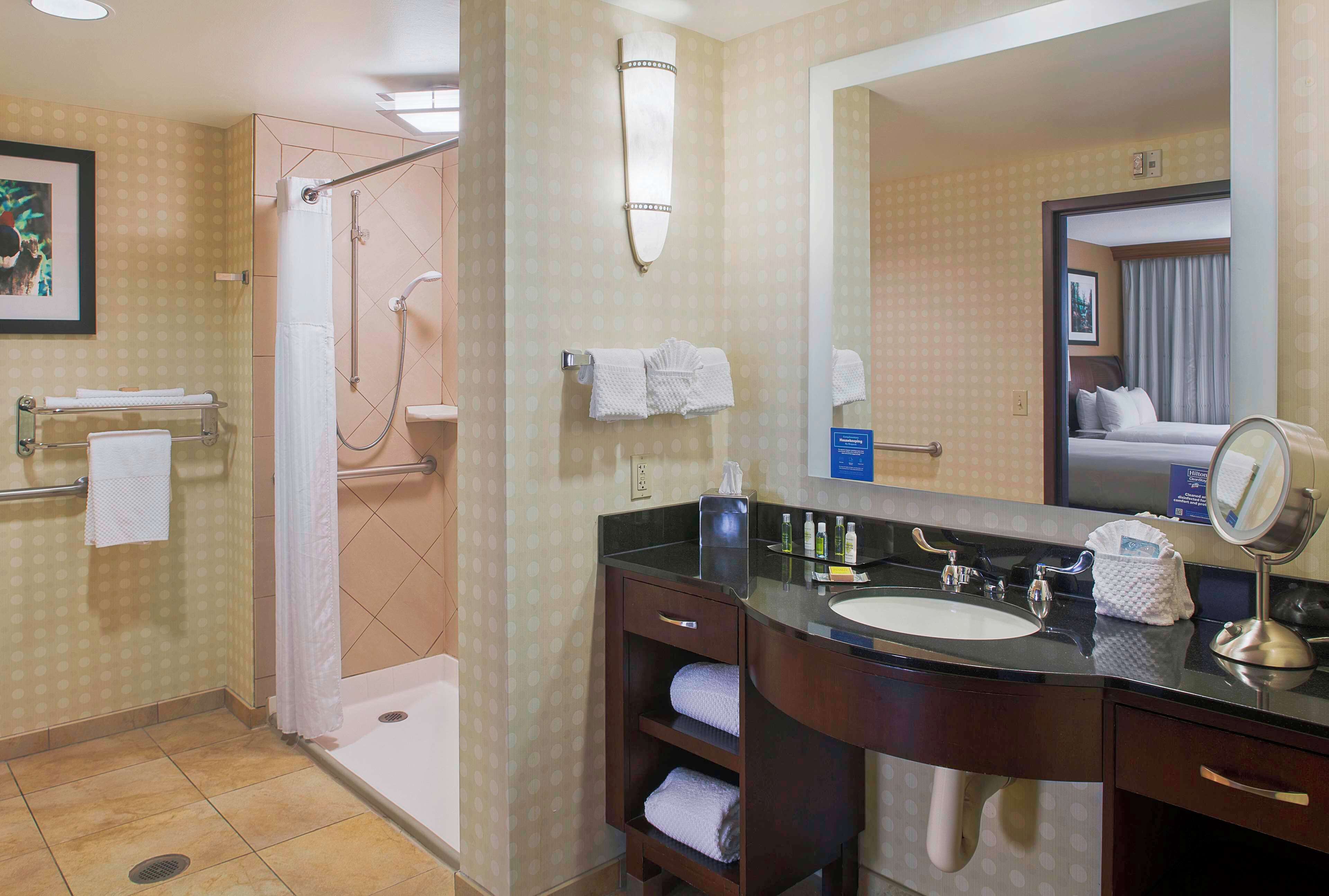Un baño de hotel con ducha, lavamanos y espejo.