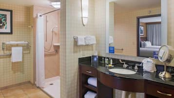 Un baño de hotel con ducha, lavamanos y espejo.