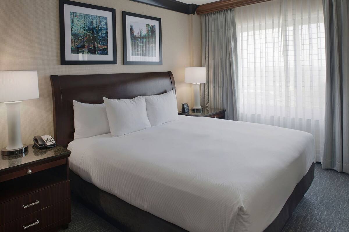 Habitación de hotel con una cama grande, dos mesitas de noche con lámparas, un teléfono y cuadros en la pared.