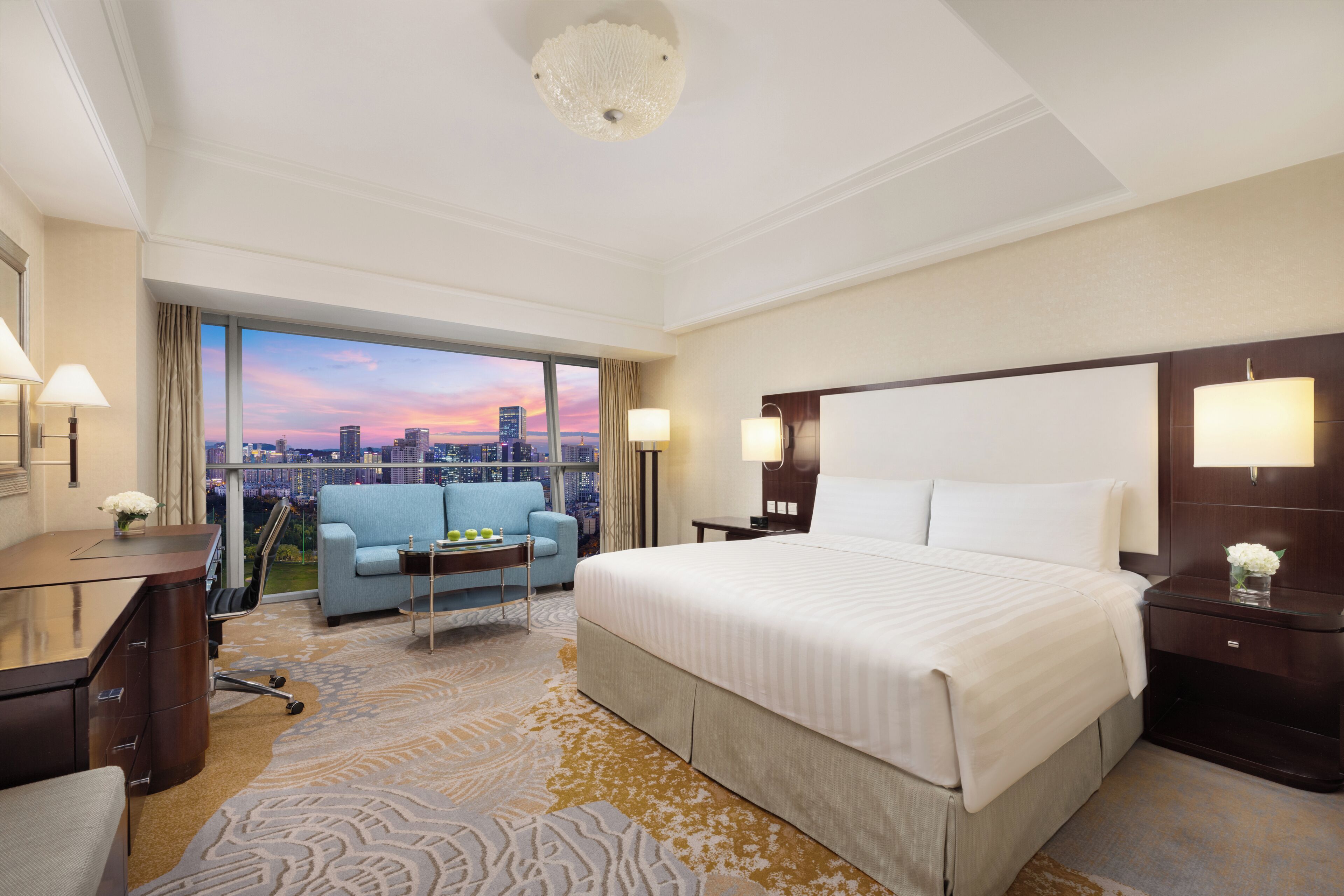 Una habitación de hotel con una cama grande, un escritorio, una silla, una mesita y vistas a la ciudad.