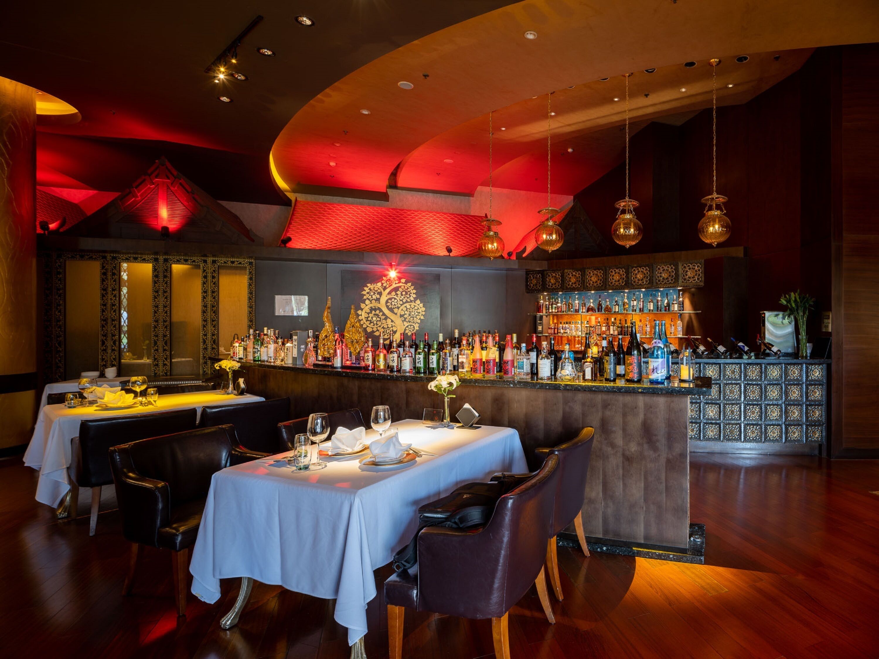 Ein Restaurant mit gedeckten Tischen, einer Bar mit Flaschen und einer Dekowand.