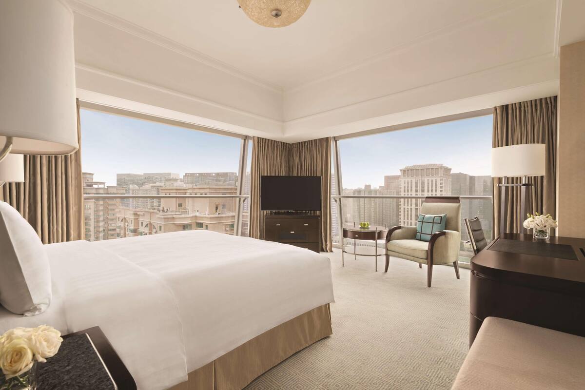 Camera d'albergo con un letto grande, una scrivania, una sedia, una TV e vista sulla città.