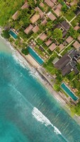 Vista aérea de un complejo turístico costero con varias cabañas tipo bungalow, una piscina central y acceso directo a la playa.