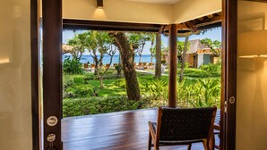 A room with a view of a tropical garden and the sea, a wooden deck, and a seating area with a bench and chairs. - Qunci Villas Resort (Senggigi)