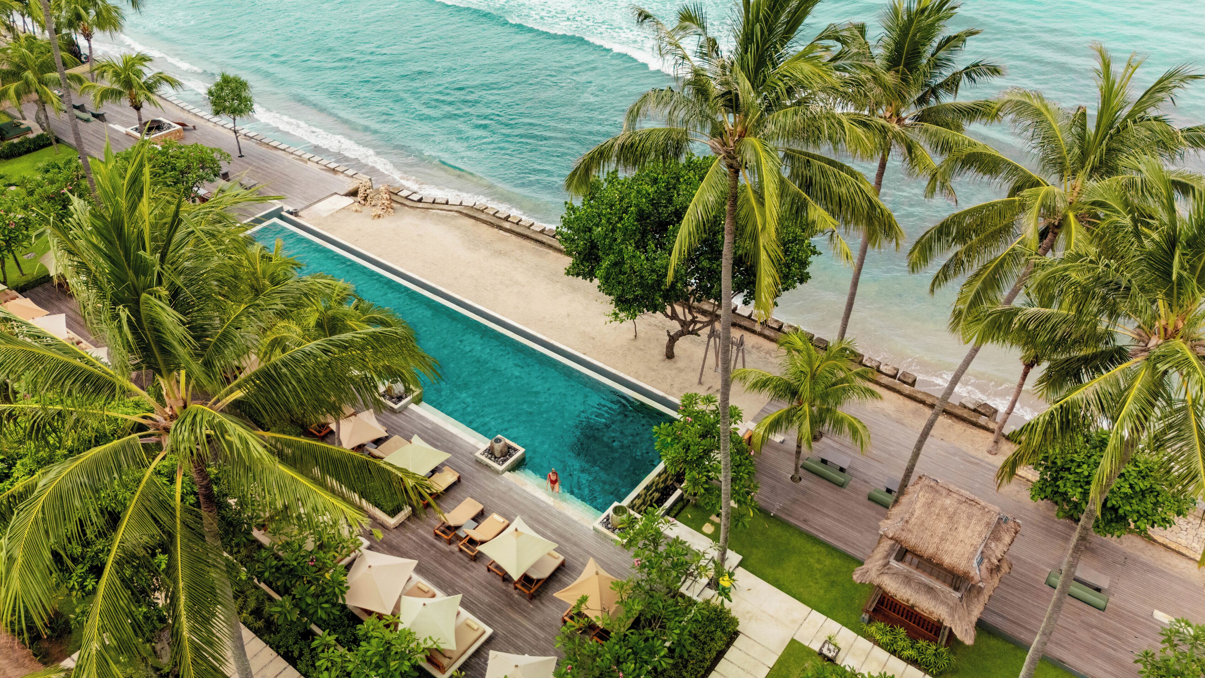 An aerial view of a resort with a swimming pool, beach, and palm trees.