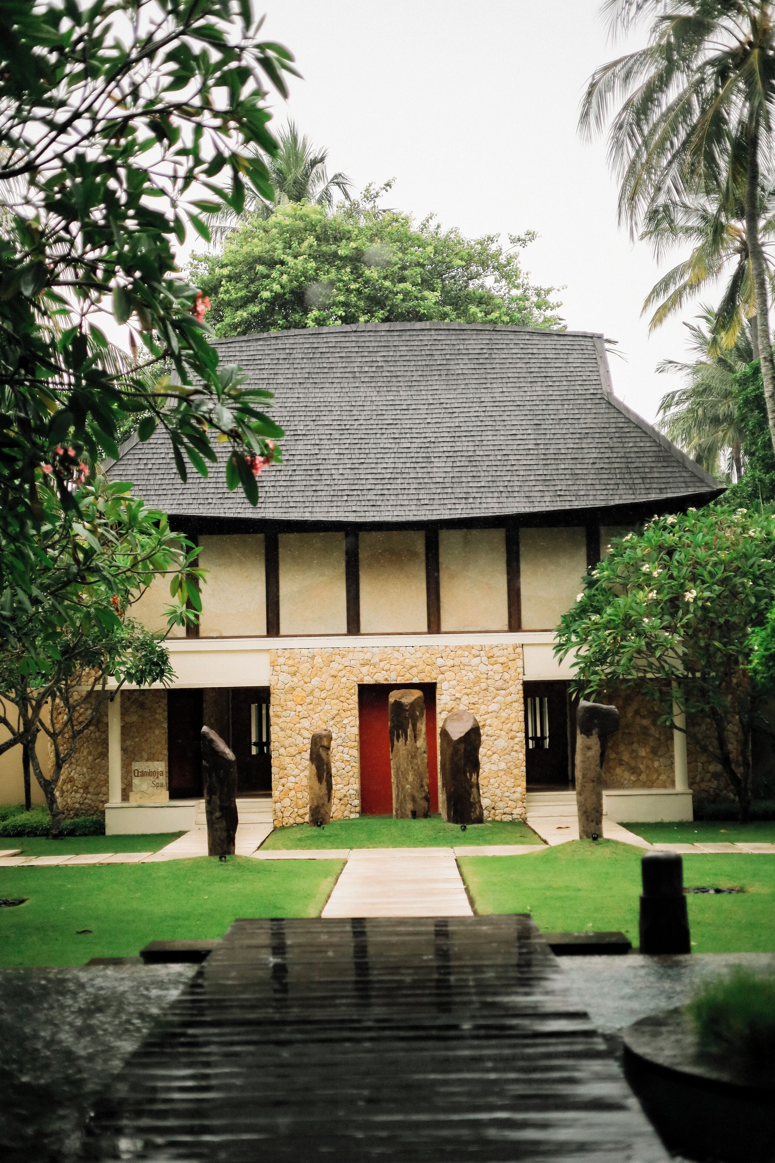 A two-story building with a stone facade, a red door, and a stone pathway leading to the entrance.