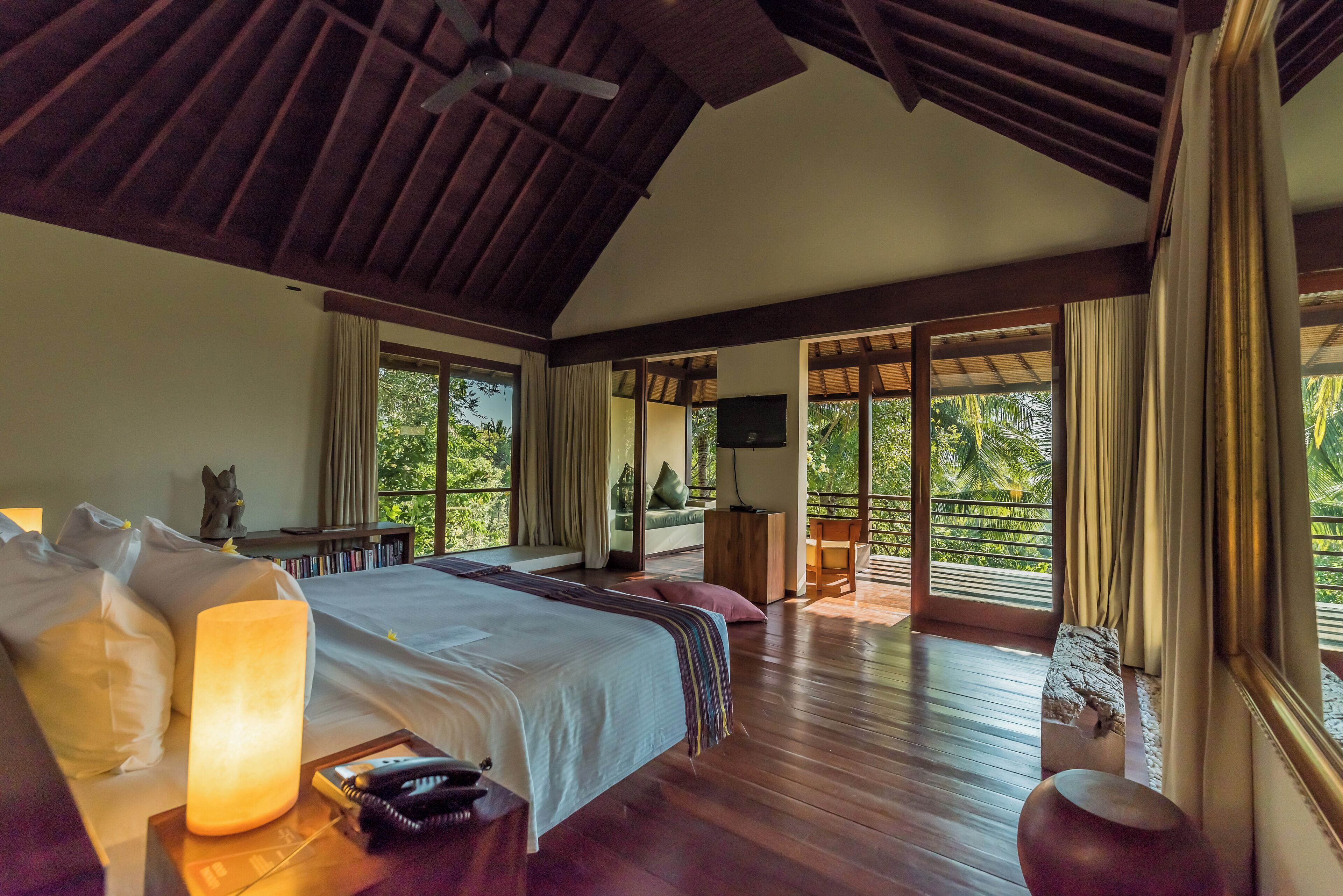 A spacious bedroom with a large bed, bedside lamps, a wooden floor, and a balcony with a view of the outdoors.