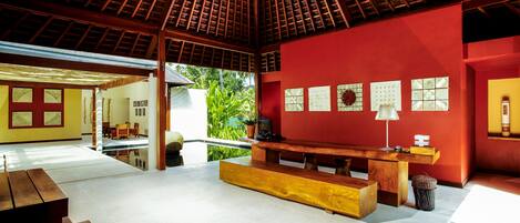 A spacious room with a wooden ceiling, a red accent wall, and a large window overlooking greenery.