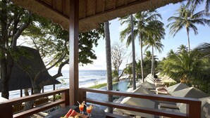 A tropical resort balcony with a table set with fruit and drinks, overlooking a pool and palm trees. - Qunci Villas Resort (Senggigi)