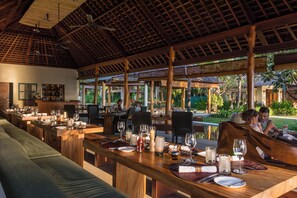 A restaurant with wooden tables and chairs, a bar area, and a view of the outdoors. - Qunci Villas Resort (Senggigi)