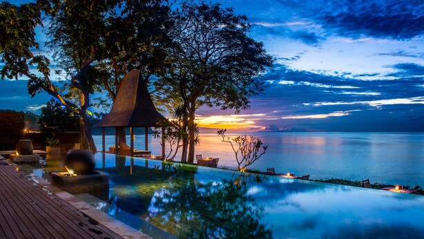 An infinity pool with a wooden deck, a gazebo, and seating areas overlooking a calm sea at sunset. - Qunci Villas Resort (Senggigi)