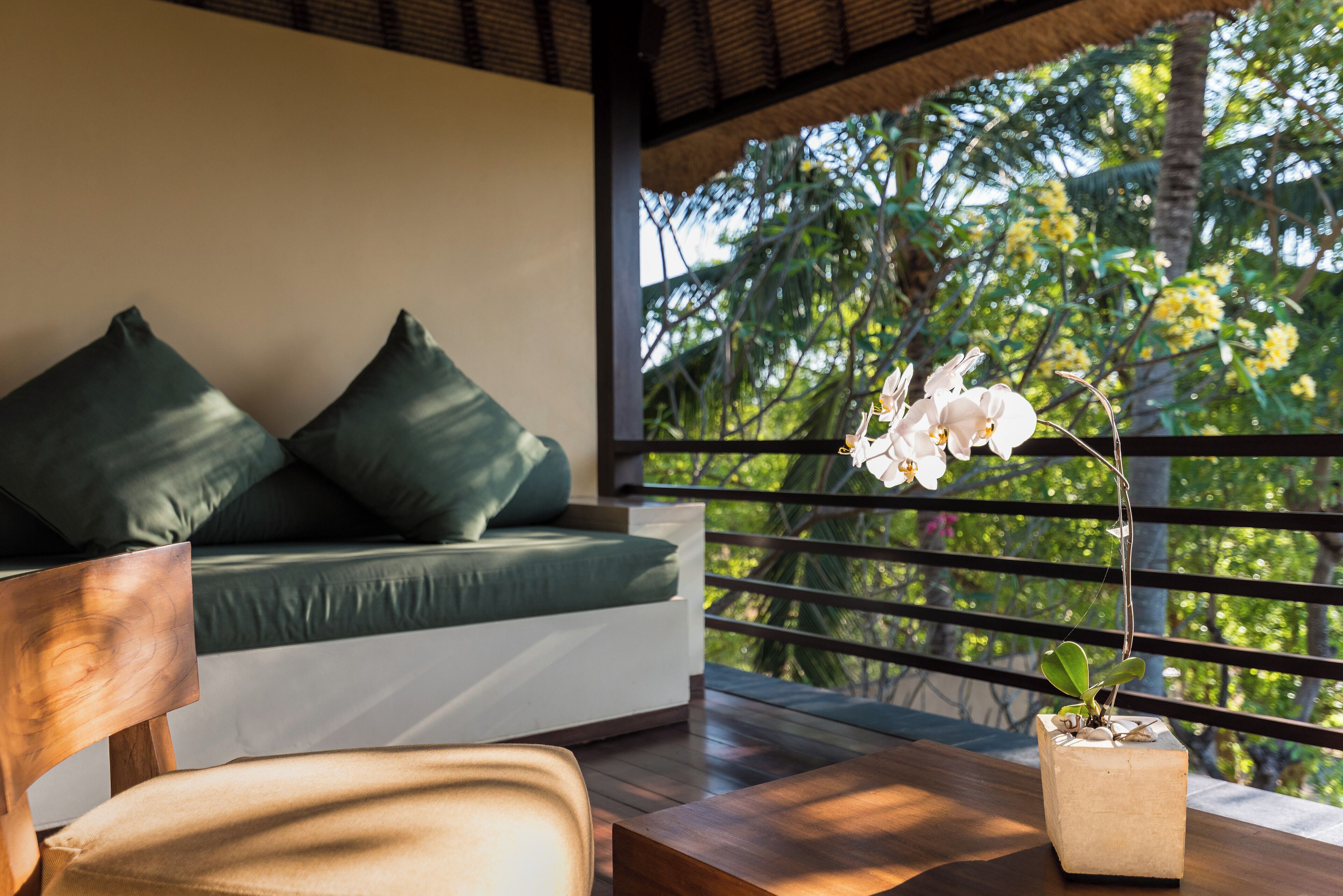 Una habitación moderna con suelo de madera, un sofá con cojines verdes, una silla de madera y una mesita con una orquídea en maceta.