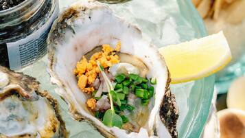 A tray of oysters on ice with lemon wedges and a jar of black olives.