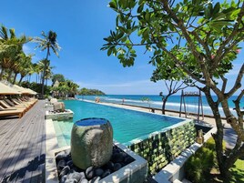 Una piscina de resort con cubierta de madera, sillas de descanso y un elemento decorativo de piedra.