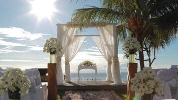 An outdoor wedding aisle with white drapery, floral arrangements, and a view of the sea.
