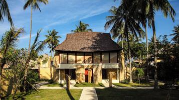 A two-story building with a thatched roof, surrounded by palm trees and a well-maintained lawn.