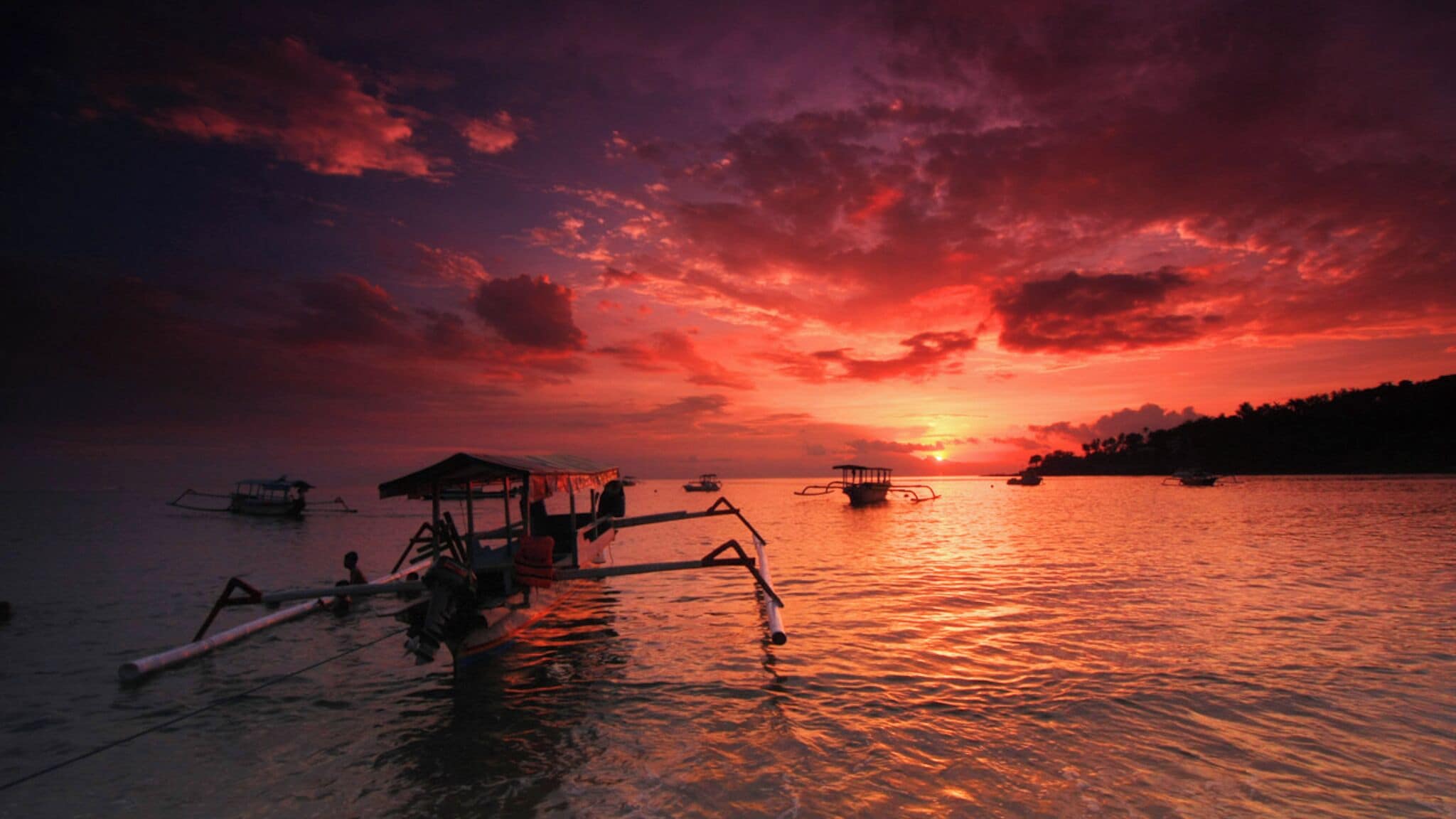 A sunset over a calm sea with boats and a dock.