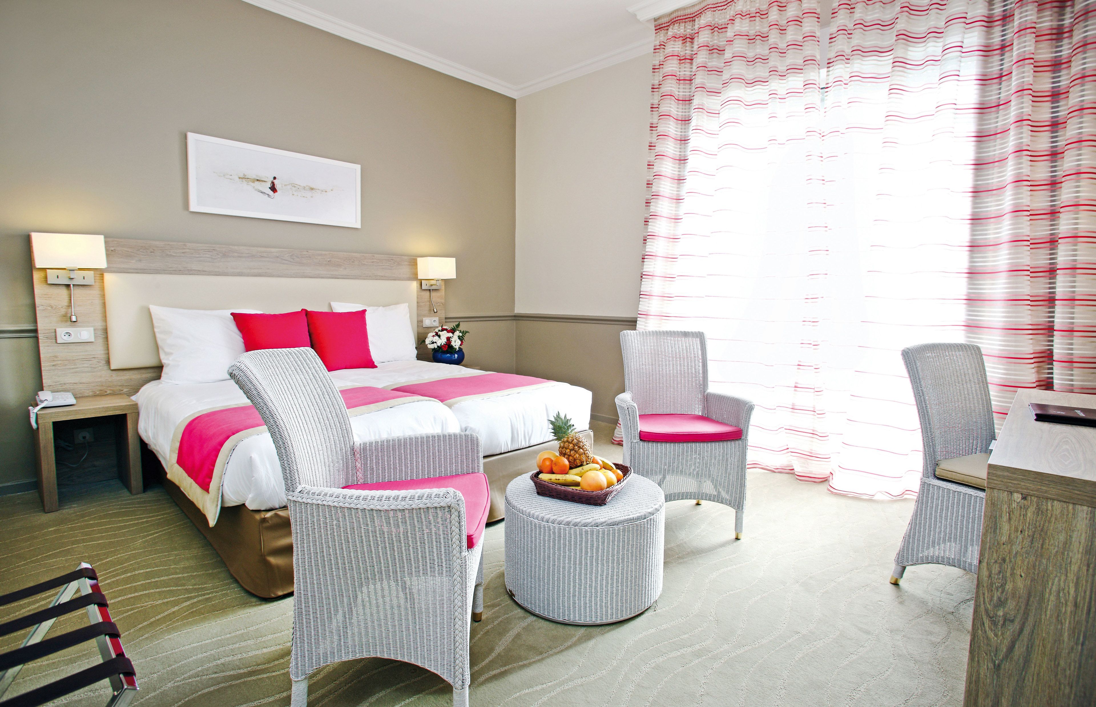 Una habitación de hotel con una cama, dos sillas, una mesita con fruta y un escritorio.