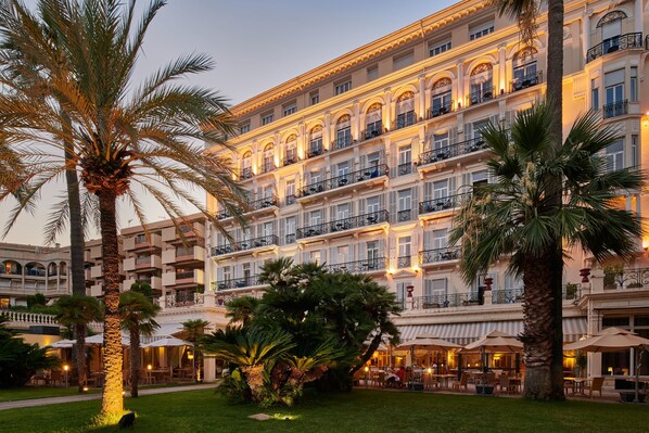A multi-story hotel with a courtyard featuring palm trees and outdoor seating.