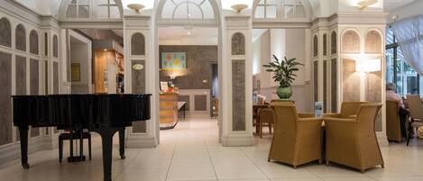 A grand lobby with a grand piano, arched doorways, and a reception desk.