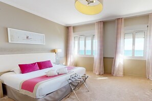 Une chambre dâhĂŽtel avec un lit, une tĂȘte de lit, une fenĂȘtre avec des rideaux, un ventilateur de plafond et un tableau au mur.
