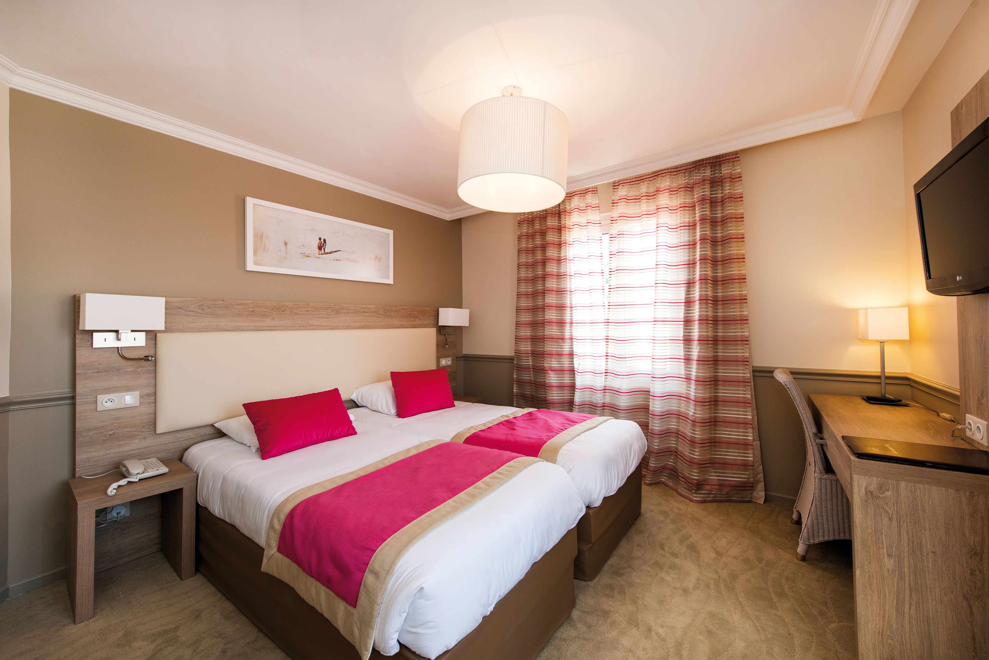 A hotel room with a large bed, two bedside tables, a desk, a television, and a window with curtains.