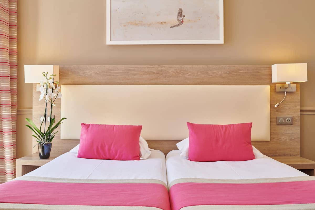 Una cama doble con ropa de cama rosa y blanca, una orquídea en maceta y una lámpara de pared.