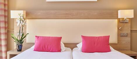 A double bed with pink and white bedding, a potted orchid, and a wall-mounted lamp.