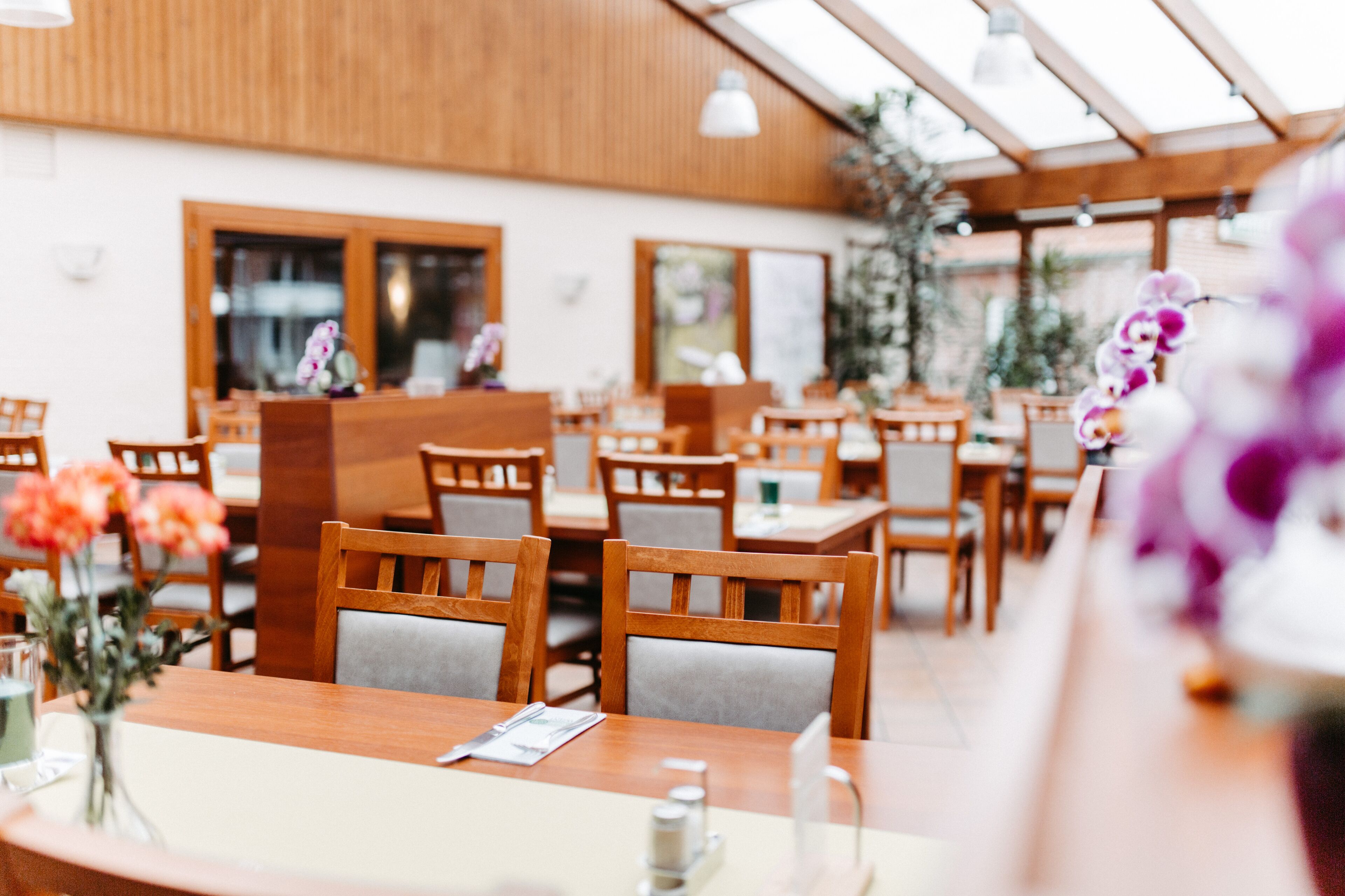 Un restaurant avec des tables et des chaises en bois, un plafond en verre et des plantes en pot.