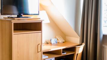 A small room with a desk, chair, television, and a telephone.