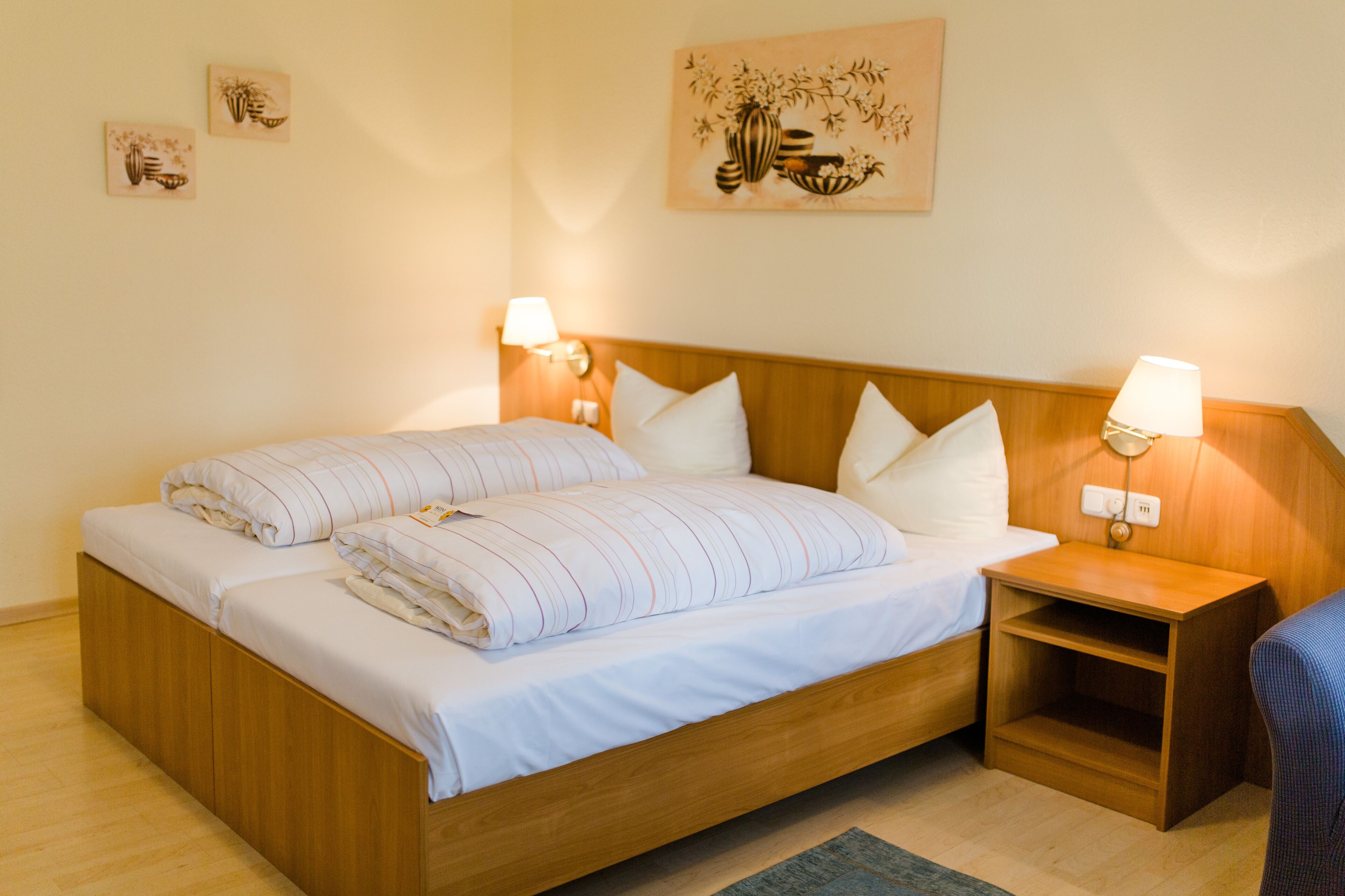 A double bed with two pillows, a wooden headboard, bedside tables with lamps, and wall art.