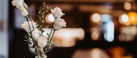 A bar area with a vase of white flowers and a candle on a counter.