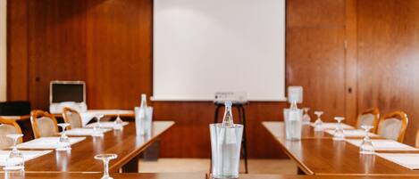 A conference room with a long wooden table, chairs, a projector screen, and a water dispenser.