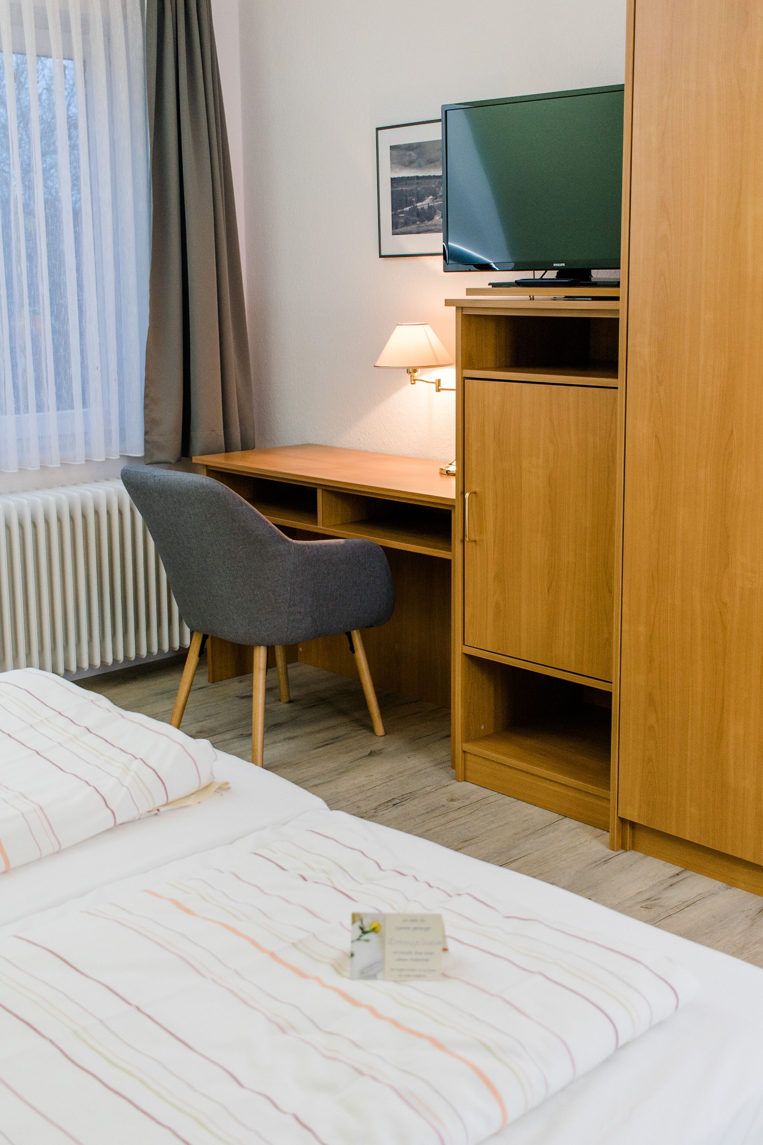 Ett hotellrum med en säng, ett skrivbord, en stol, en tv och en lampa.