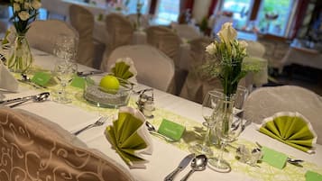 A formal dining setup with neatly arranged tables, chairs, and a chandelier.