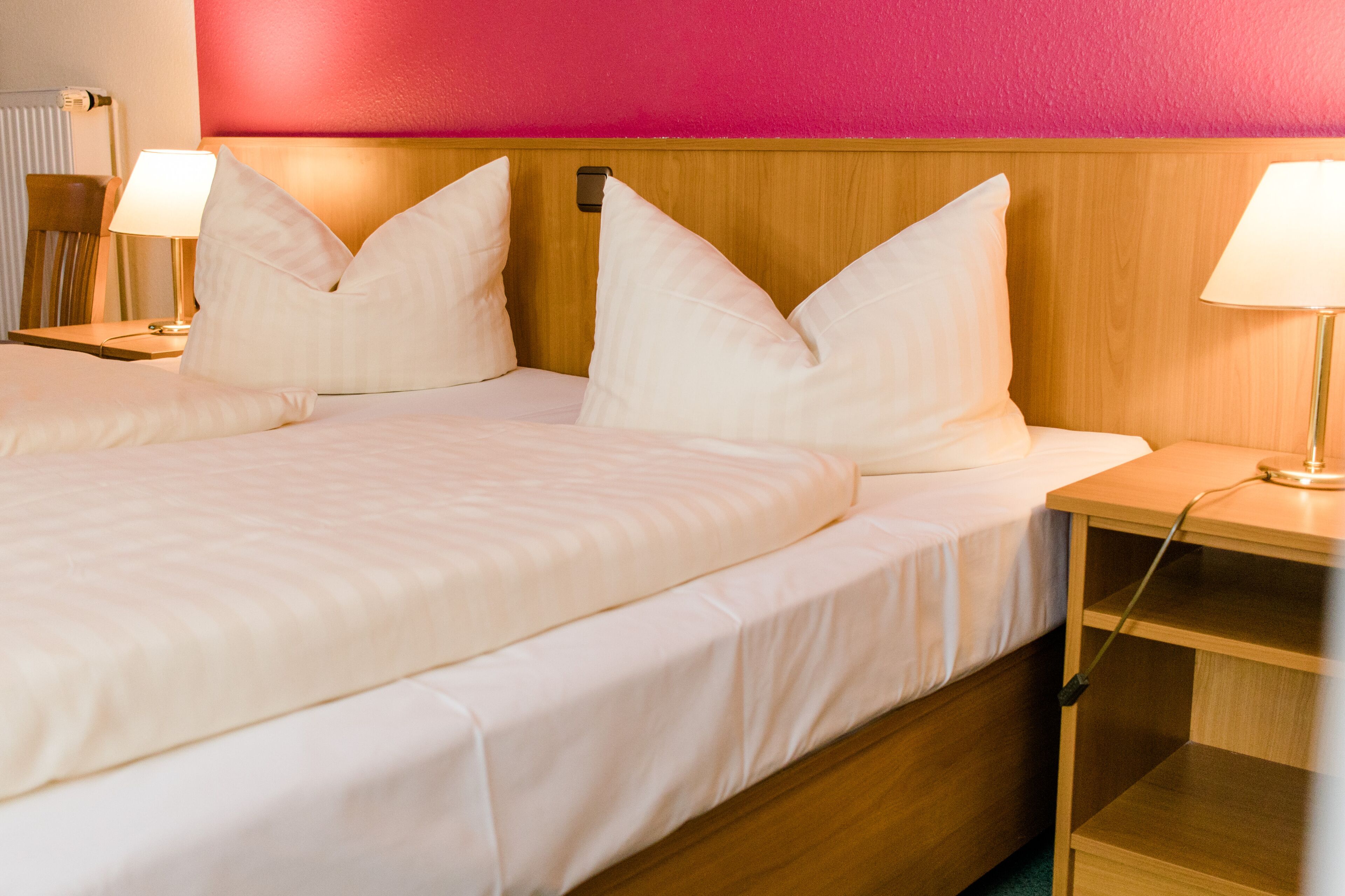 Ein Doppelbett mit weißer Bettwäsche, ein Holz-Kopfstück und Nachttische mit Lampen.