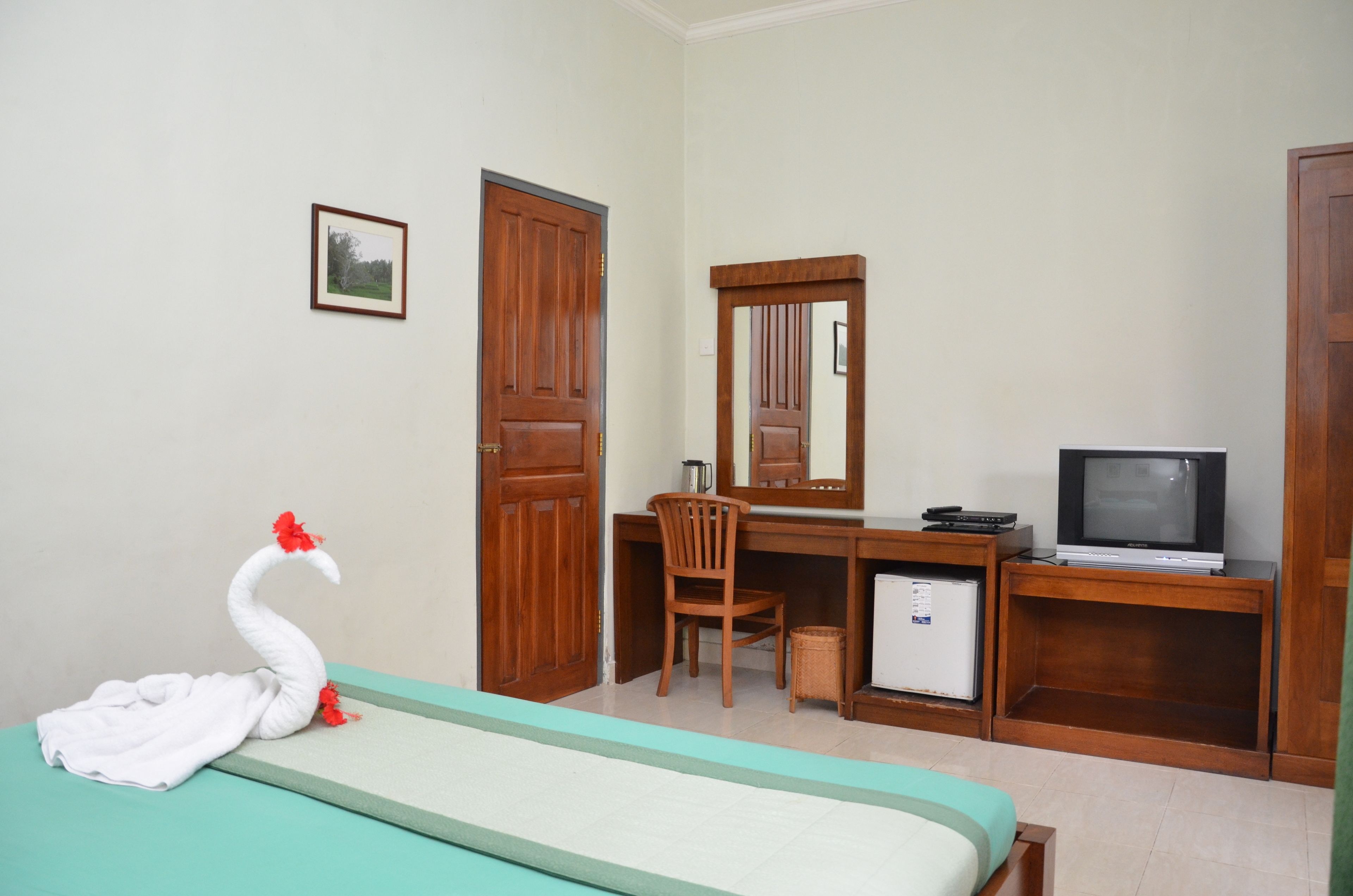 A hotel room with a bed, a desk with a chair, a television, and a small refrigerator.