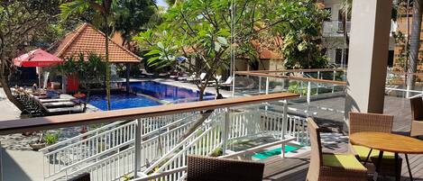 A pool area with lounge chairs and umbrellas, surrounded by tropical plants and a wooden deck.