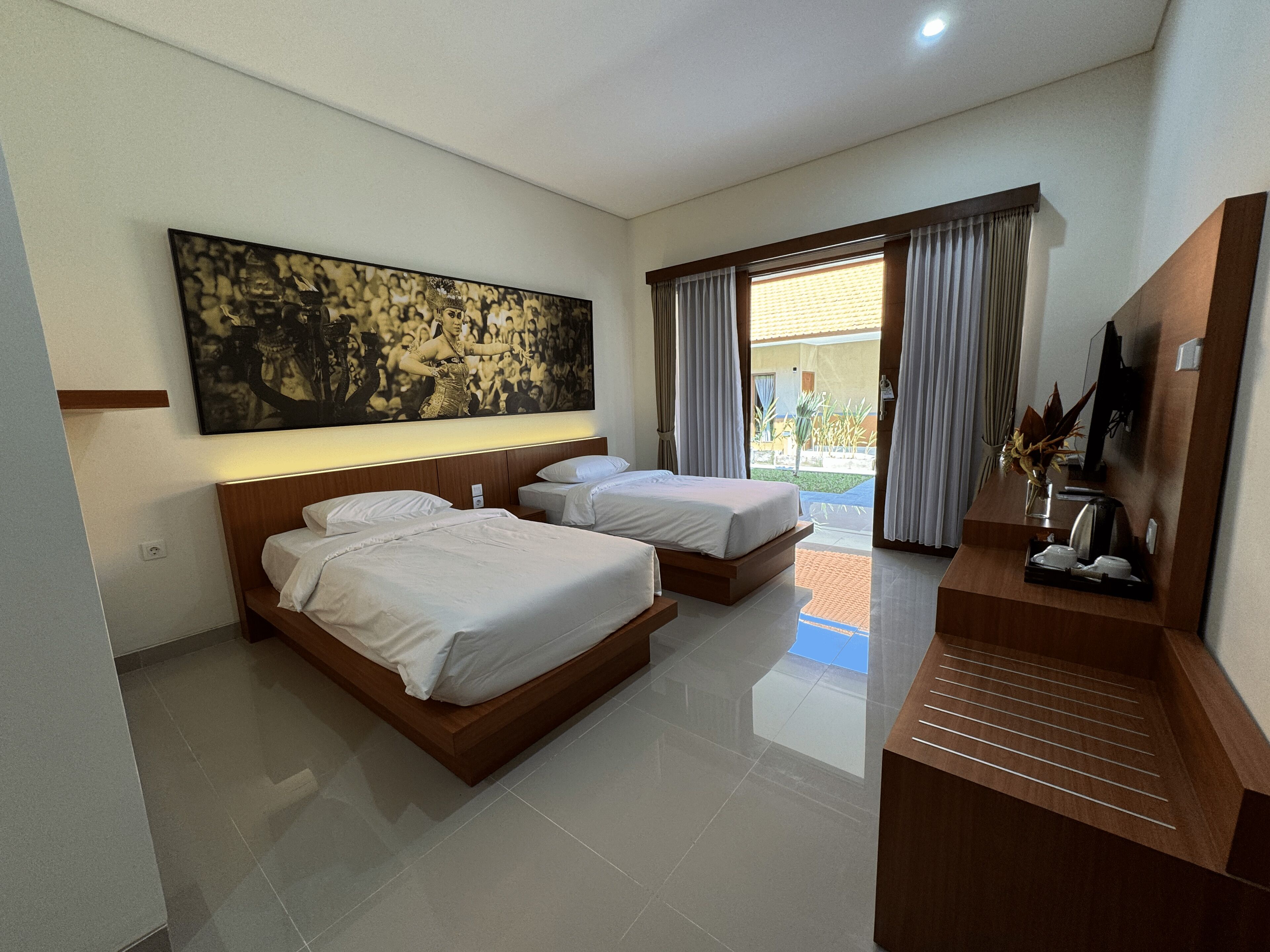 A hotel room with two beds, a large artwork on the wall, a TV, and a view of the outdoor area.
